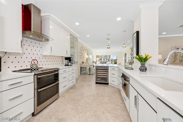 kitchen featuring white cabinets, wall chimney range hood, sink, stainless steel appliances, and beverage cooler