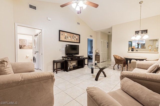 tiled living room featuring ceiling fan with notable chandelier, stacked washer and dryer, and high vaulted ceiling