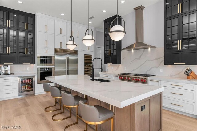 kitchen with wine cooler, a spacious island, sink, wall chimney range hood, and decorative light fixtures