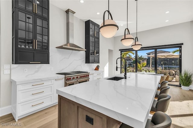 kitchen with sink, wall chimney exhaust hood, decorative backsplash, range with two ovens, and pendant lighting