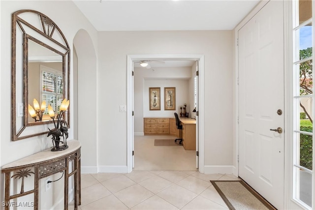 entryway with arched walkways, a wealth of natural light, built in desk, and light tile patterned floors