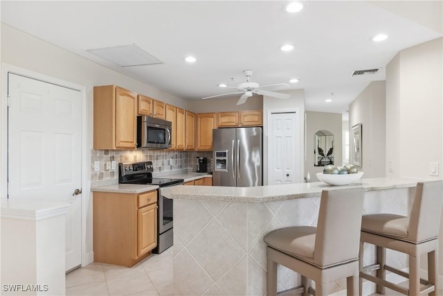 kitchen featuring visible vents, a breakfast bar area, a peninsula, stainless steel appliances, and backsplash