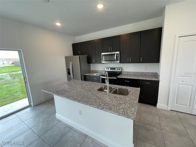 kitchen with light stone countertops, an island with sink, light tile patterned floors, and appliances with stainless steel finishes