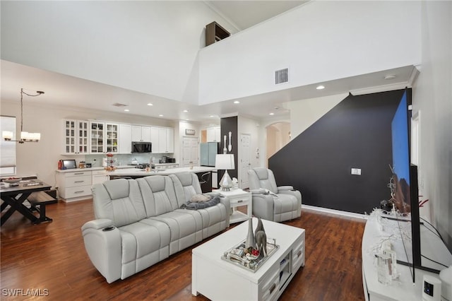 living room featuring a notable chandelier, dark hardwood / wood-style flooring, a towering ceiling, and ornamental molding