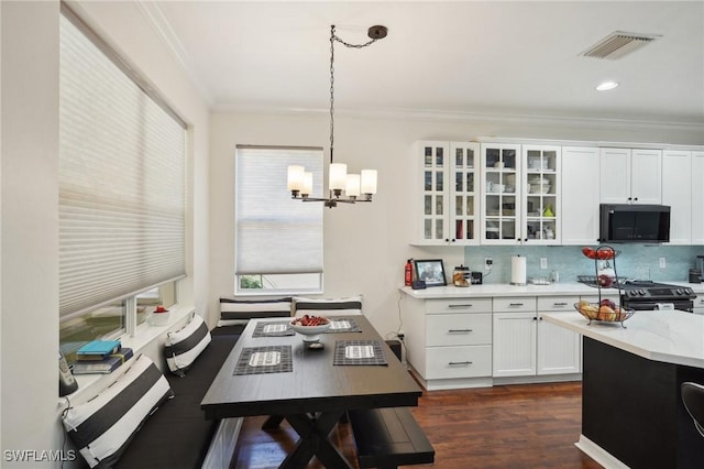 kitchen with black stove, decorative light fixtures, ornamental molding, a notable chandelier, and white cabinetry