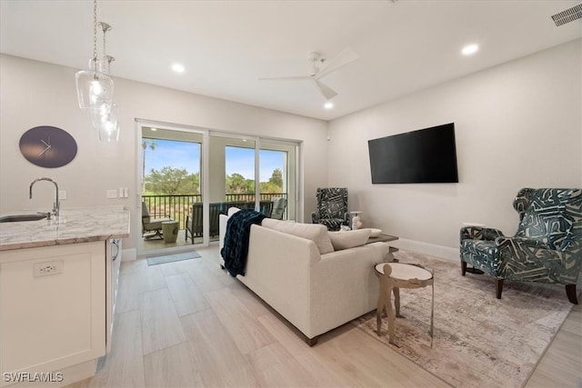 living room featuring light hardwood / wood-style flooring, ceiling fan, and sink