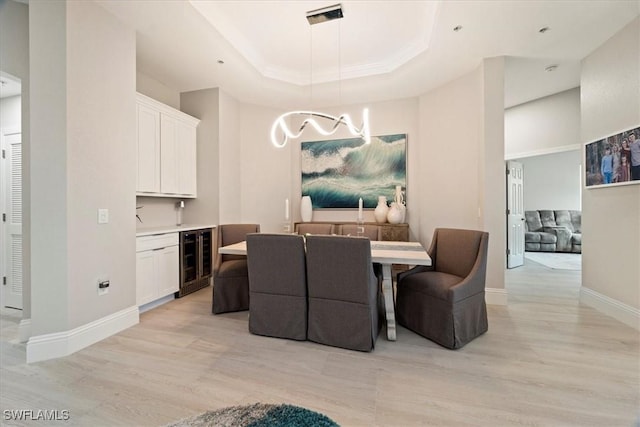 dining space with light hardwood / wood-style floors, a raised ceiling, and beverage cooler