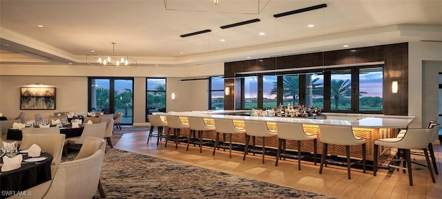 bar with a tray ceiling, a wealth of natural light, an inviting chandelier, and light wood-type flooring