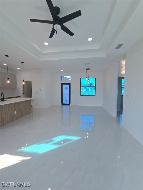 unfurnished living room with a tray ceiling, ceiling fan, and sink