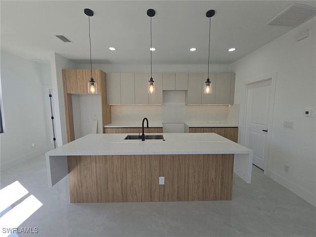 kitchen with white cabinetry, sink, hanging light fixtures, and an island with sink