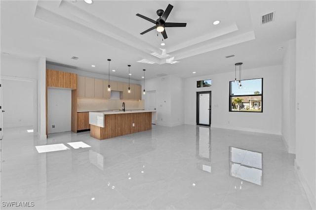 kitchen with sink, hanging light fixtures, a kitchen island with sink, ceiling fan, and a tray ceiling