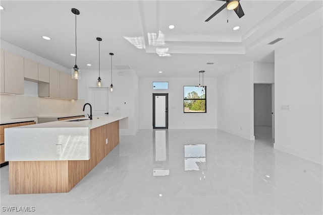 kitchen with light brown cabinetry, sink, tasteful backsplash, hanging light fixtures, and a large island with sink