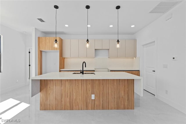 kitchen featuring pendant lighting, tasteful backsplash, sink, white cabinets, and a center island with sink