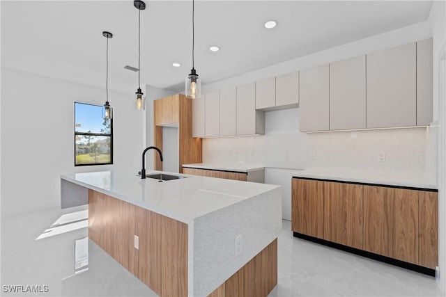 kitchen with sink, white cabinetry, hanging light fixtures, an island with sink, and backsplash