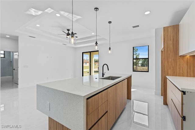 kitchen featuring decorative light fixtures, white cabinetry, sink, a large island with sink, and a raised ceiling