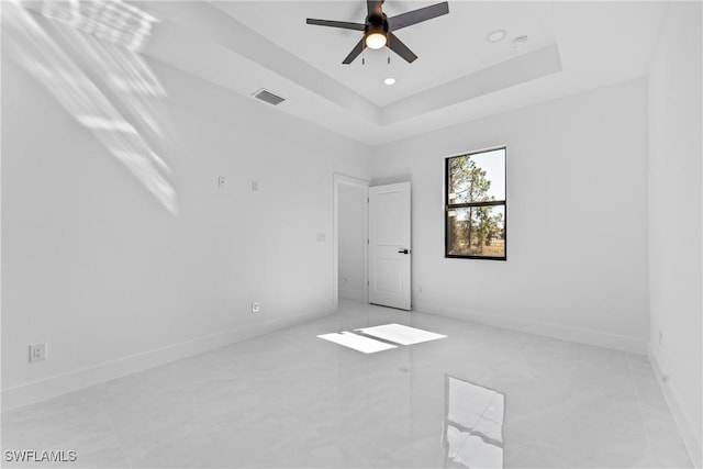 empty room with ceiling fan and a tray ceiling