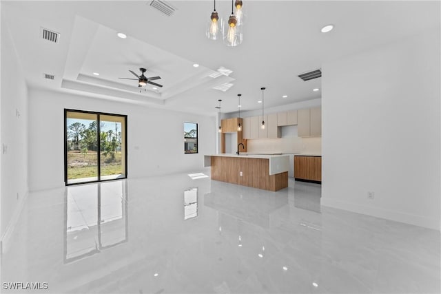 unfurnished living room featuring sink, a tray ceiling, and ceiling fan