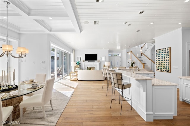 kitchen featuring light stone counters, pendant lighting, light hardwood / wood-style floors, white cabinetry, and a kitchen breakfast bar