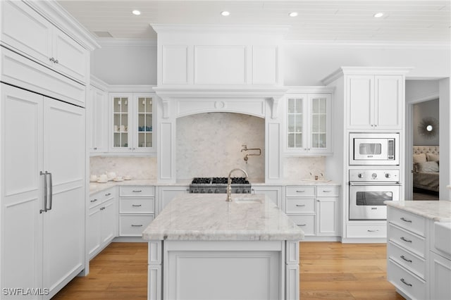 kitchen featuring an island with sink, built in appliances, light stone countertops, decorative backsplash, and white cabinetry