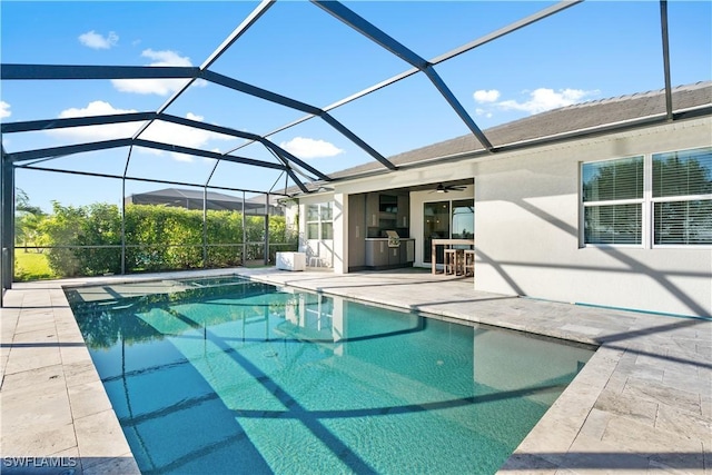 view of swimming pool featuring an outdoor kitchen, glass enclosure, a patio, and ceiling fan