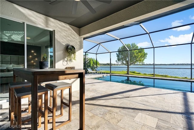 view of patio featuring a lanai, ceiling fan, a water view, and a bar