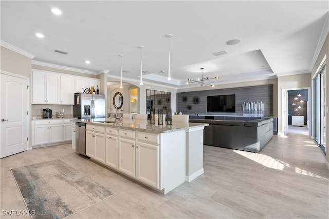 kitchen featuring stainless steel appliances, a raised ceiling, sink, white cabinetry, and an island with sink