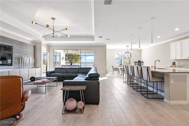 living room featuring a raised ceiling, crown molding, a notable chandelier, and sink