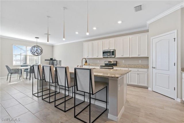 kitchen with white cabinetry, light stone countertops, stainless steel appliances, decorative light fixtures, and a kitchen island with sink