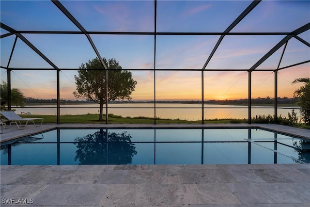 pool at dusk featuring a lanai, a patio area, and a water view