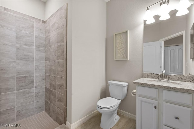 bathroom with tiled shower, hardwood / wood-style floors, vanity, and toilet