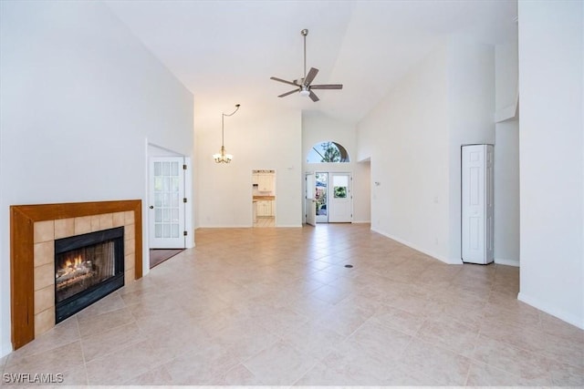 unfurnished living room with a tile fireplace, ceiling fan with notable chandelier, and high vaulted ceiling