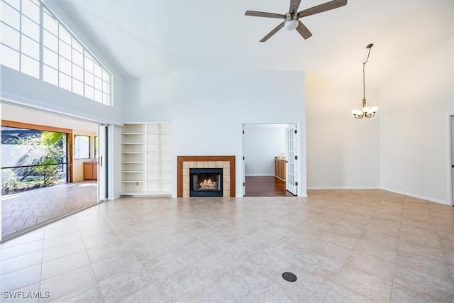 unfurnished living room with a tile fireplace, built in shelves, a towering ceiling, light tile patterned floors, and ceiling fan with notable chandelier