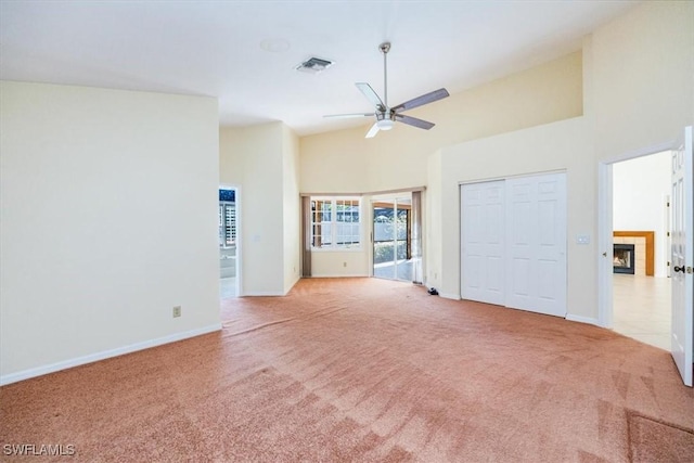 unfurnished living room with light carpet, a fireplace, ceiling fan, and high vaulted ceiling