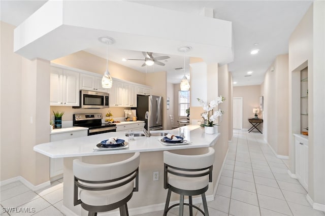 kitchen featuring a breakfast bar, white cabinets, ceiling fan, light tile patterned floors, and appliances with stainless steel finishes