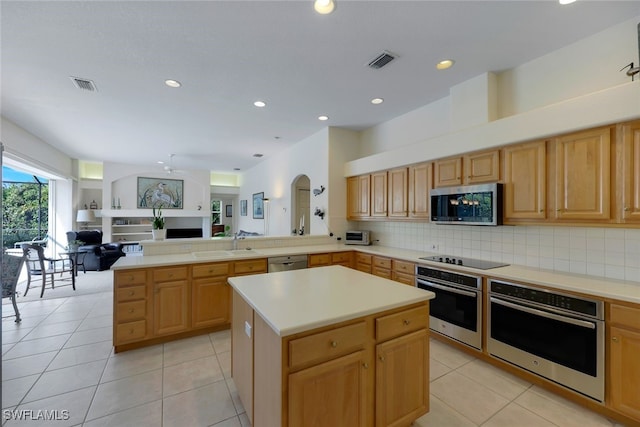 kitchen with light tile patterned floors, tasteful backsplash, kitchen peninsula, a kitchen island, and appliances with stainless steel finishes