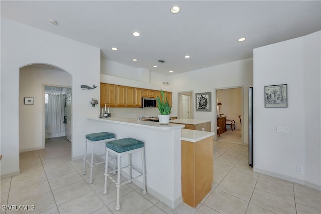 kitchen with kitchen peninsula, light tile patterned floors, tasteful backsplash, and a kitchen breakfast bar