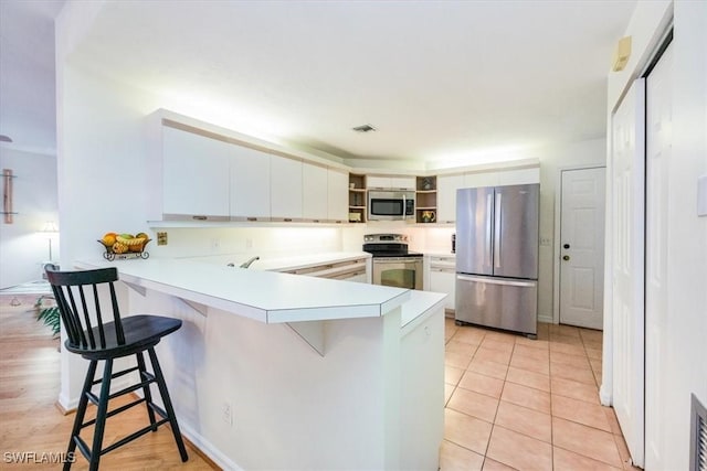 kitchen with kitchen peninsula, appliances with stainless steel finishes, a breakfast bar, and white cabinets