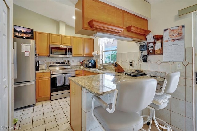 kitchen with a kitchen breakfast bar, kitchen peninsula, appliances with stainless steel finishes, and sink