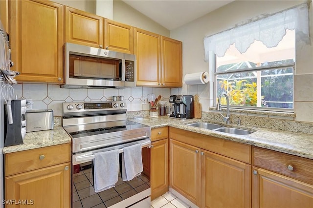 kitchen featuring light tile patterned floors, appliances with stainless steel finishes, backsplash, lofted ceiling, and sink