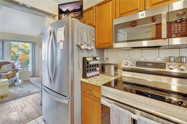 kitchen featuring decorative backsplash, light stone countertops, and stainless steel appliances