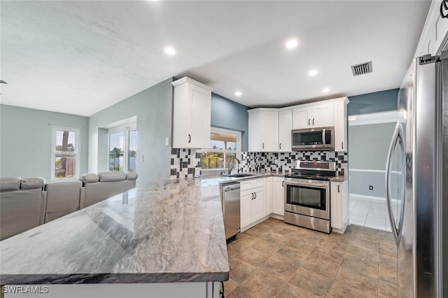 kitchen with sink, appliances with stainless steel finishes, white cabinetry, light stone counters, and tasteful backsplash