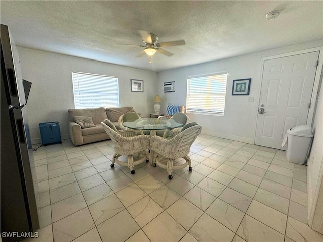 dining space with a textured ceiling, light tile patterned floors, a wall unit AC, a ceiling fan, and baseboards