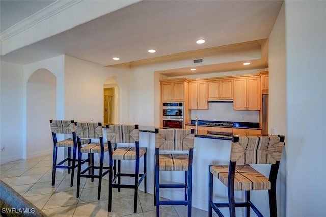 kitchen with a breakfast bar, extractor fan, light tile patterned floors, light brown cabinets, and appliances with stainless steel finishes