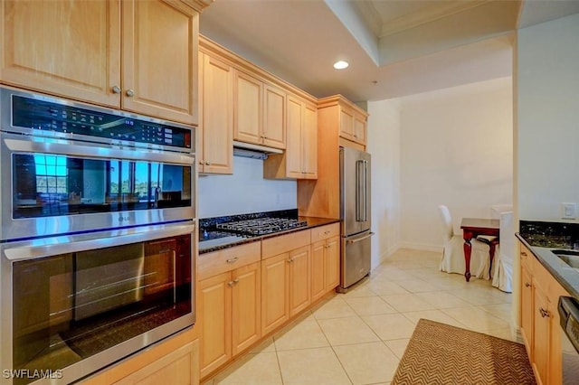 kitchen featuring light tile patterned flooring, light brown cabinetry, dark stone countertops, ornamental molding, and appliances with stainless steel finishes