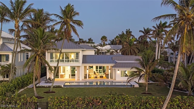 back house at dusk with a swimming pool with hot tub, a yard, a balcony, and a patio