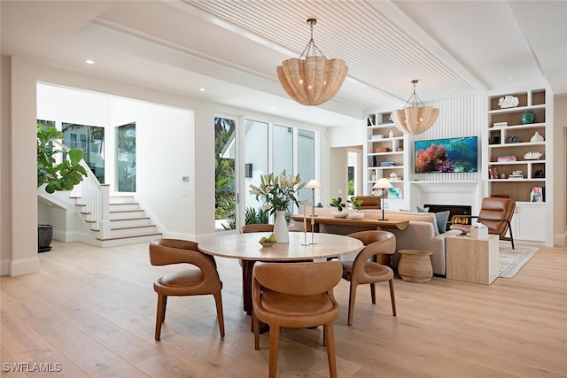 dining area with built in shelves, light hardwood / wood-style flooring, and a chandelier