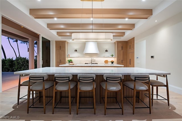 kitchen with exhaust hood, a large island, pendant lighting, light hardwood / wood-style flooring, and a breakfast bar area