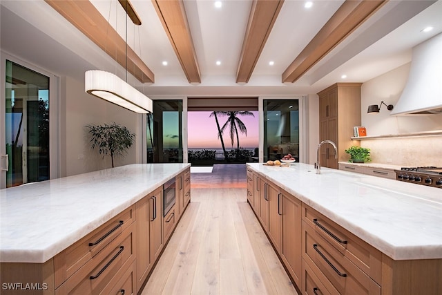 55 13th Ave S, Naples, FL 34102 - kitchen with a spacious island, light wood-style floors, custom exhaust hood, a sink, and light stone countertops