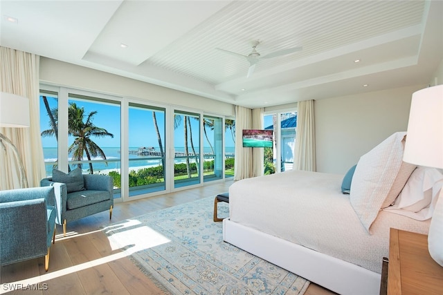 bedroom with ceiling fan, wood-type flooring, access to outside, multiple windows, and a water view