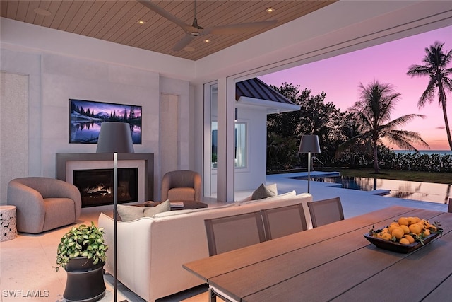 patio terrace at dusk with ceiling fan and an outdoor fireplace